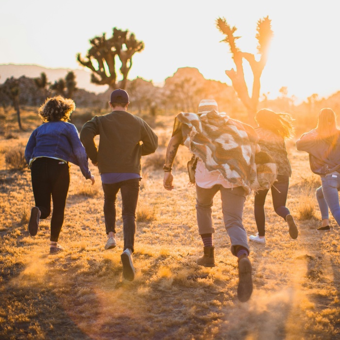 a group of young adults running towards a brown landscape with trees silhouetted in the distance