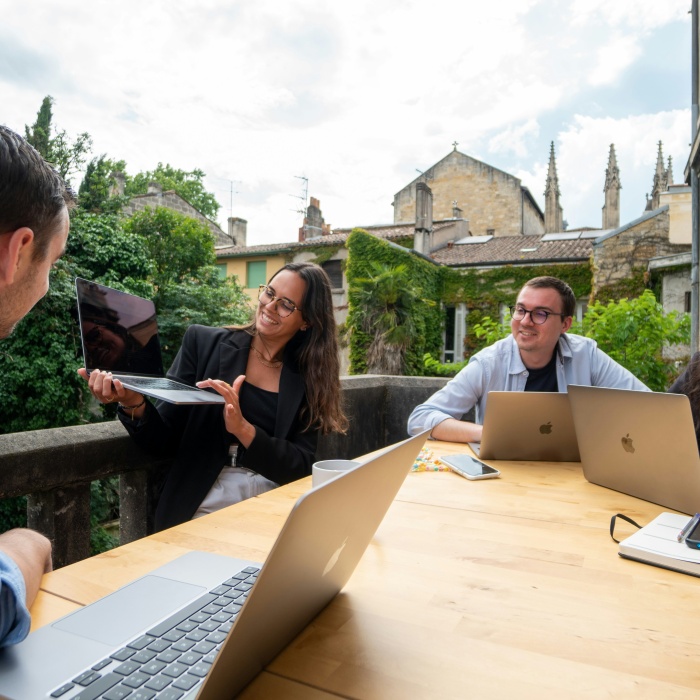 four young adults seated outdoors at a table and looking at a laptop