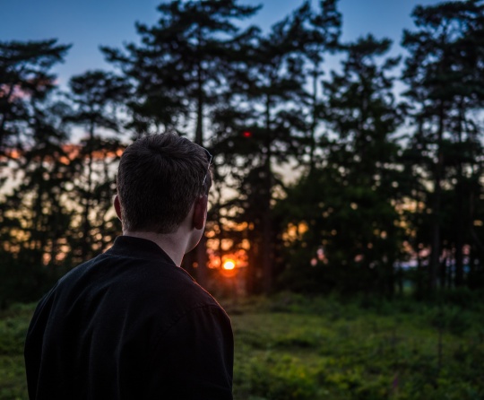 A man outside with the sun behind the trees.