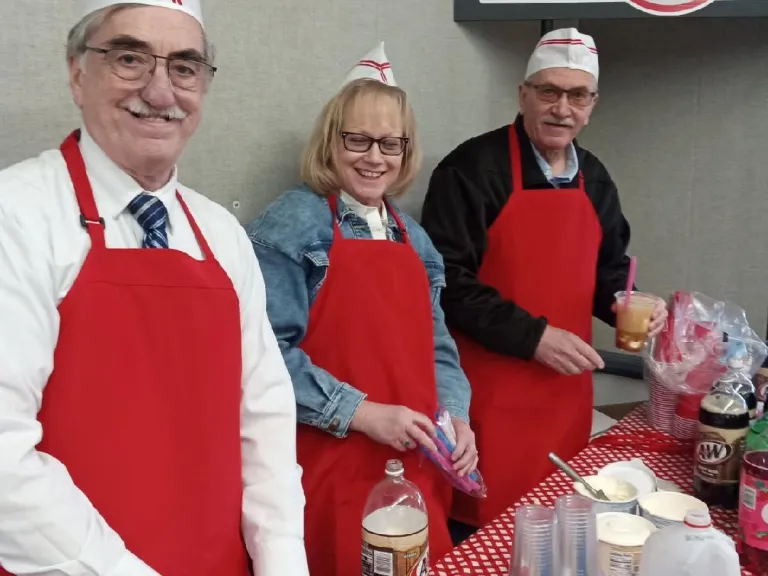 Churches Combine for 1950s Social three people dressed in a fast food uniform preparing food