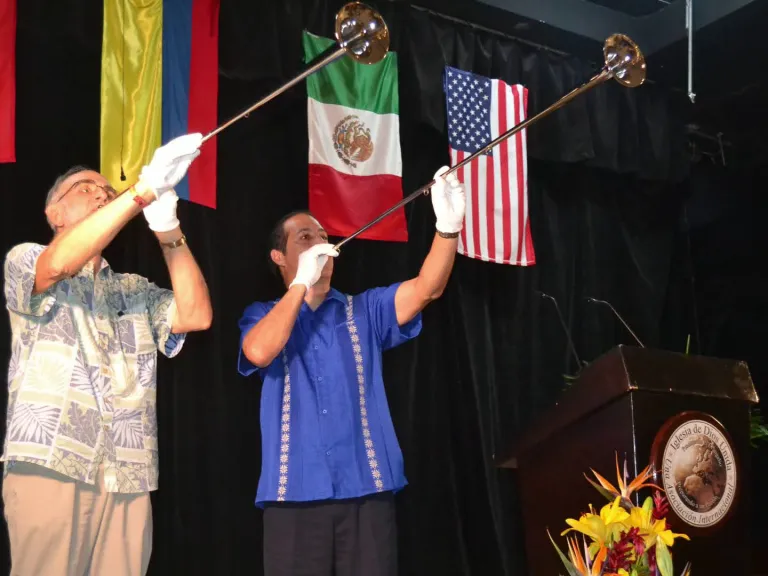 Men blowing horns against a backdrop of various countries' flags