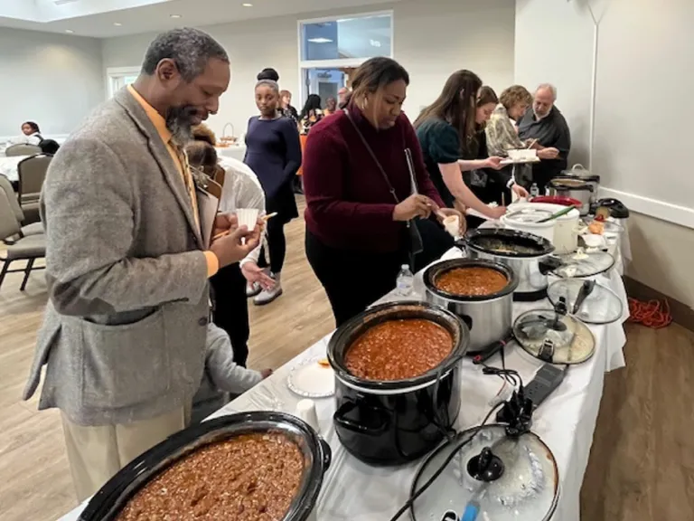 Judges evaluate the chili for the contest. people standing over crockpots and taking notes