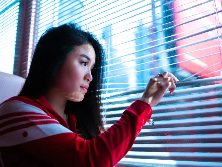 a woman looking outdoors through the window blinds