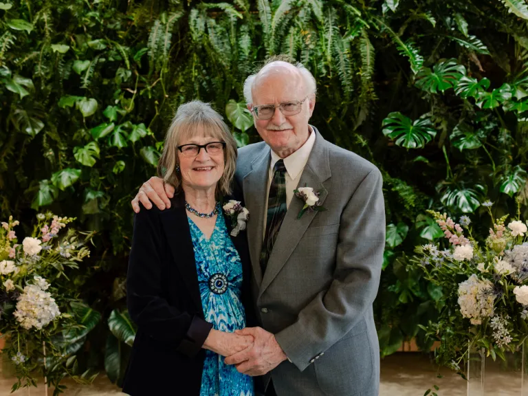 a man and a woman standing in front of greenery