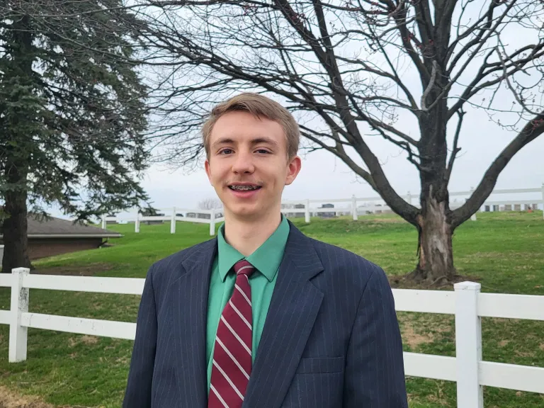 a teenager standing outside in front of a white fence