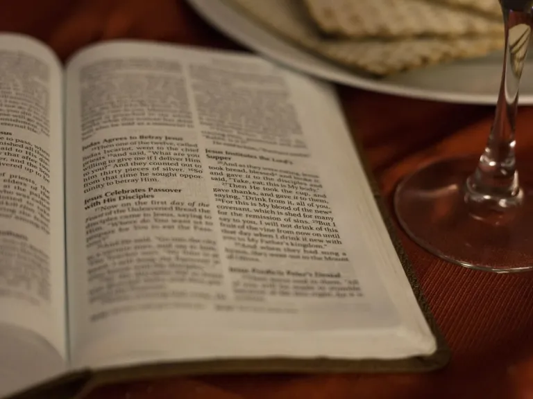 How does this festival teach us about Jesus Christ? an open Bible on a table with matzos and a glass of wine.