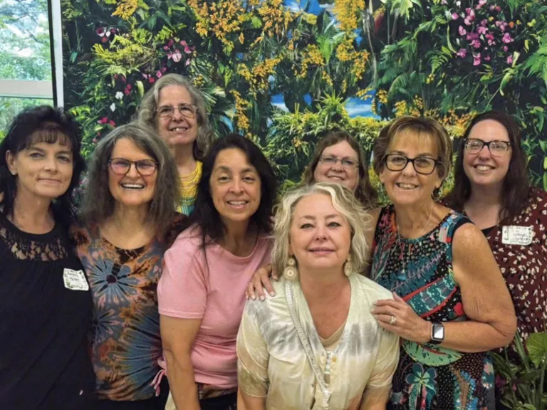 8 women standing in front of a floral backdrop