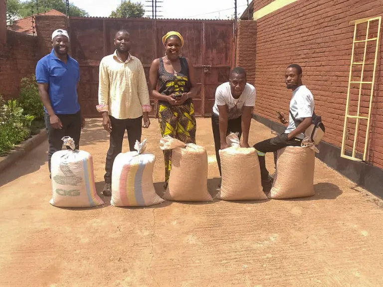 Recipients of maize in Malawi five people outdoors in a courtyard with bags of maize