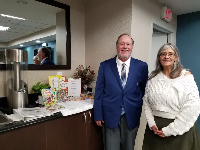 Pastor Joe Greene and Kathy Shafer stand beside Children’s Corner table. two people standing beside a table with a mirror