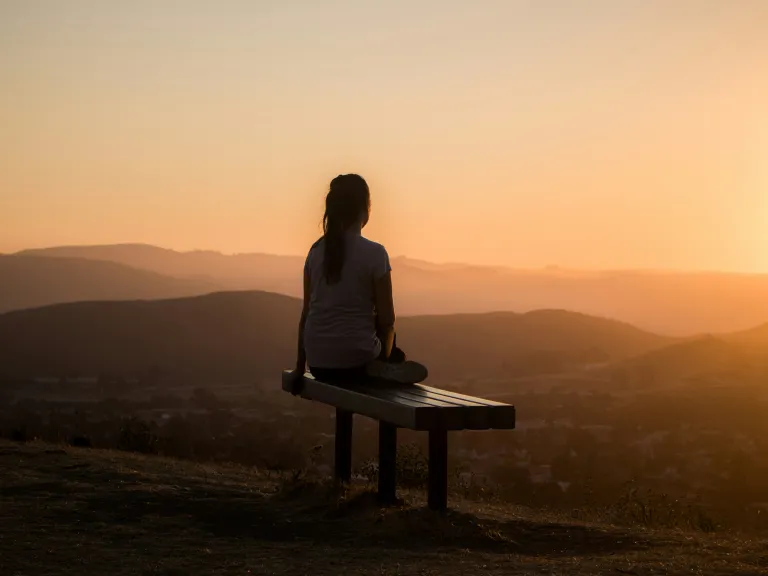 We will be happy when we follow God’s laws, delight in God’s instruction and meditate on it day and night, and keep God’s decrees and seek Him with all our heart. A young woman sitting on a bench looking out over a vista of rolling hills.