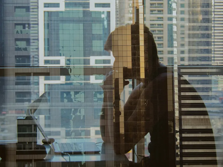 The reflection of man sitting and staring at his laptop computer.