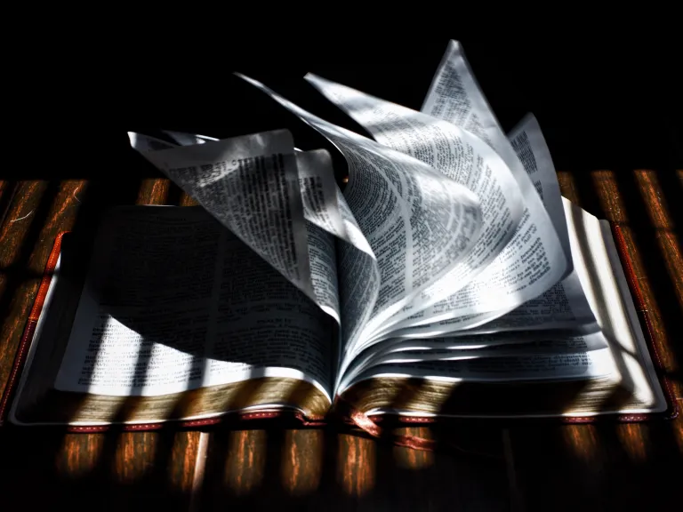 God has ultimate control over His creation, and Satan can do no more than God allows as He works out His great purpose, allowing humanity to learn important lessons. A Bible laying on table and the pages are blowing in a breeze.
