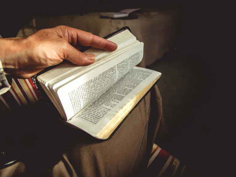 A man holding a Bible on its lap flipping through pages.