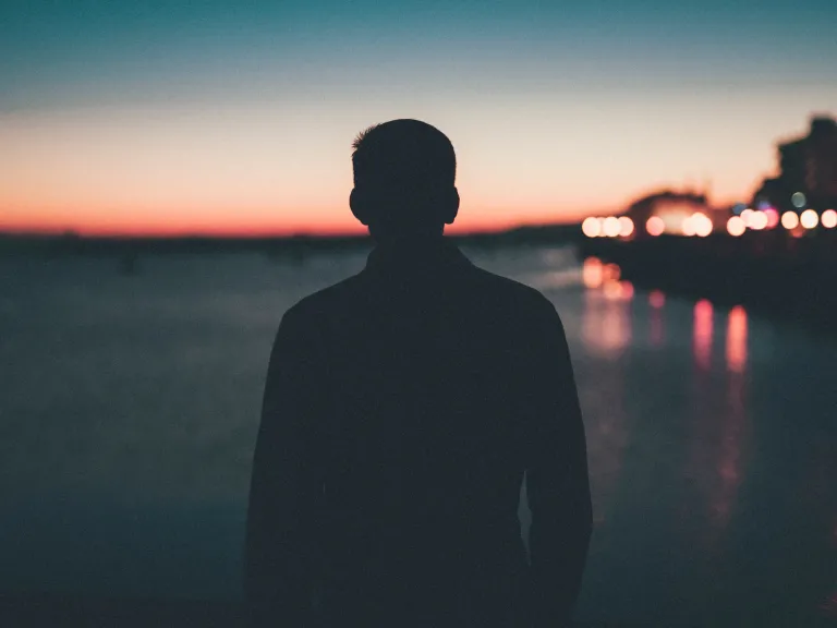 A silhouette of young man looking out over a body of water.