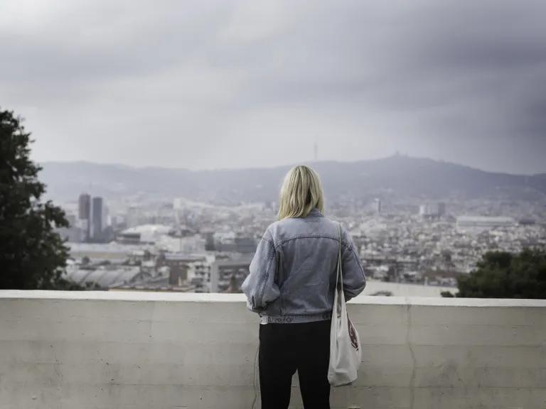 How often do we lie to ourselves and not even know it? A woman standing by a brick wall looking out over city buildings.