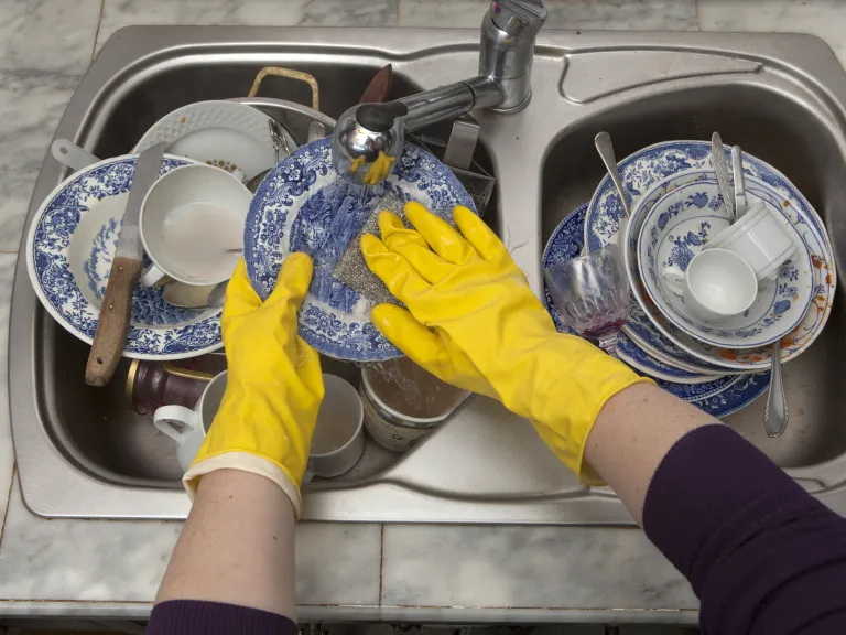 Jesus used the metaphor of cleaning dishes: “First wash the inside of the cup and the dish, and then the outside will become clean, too.” A person wearing yellow dish gloves and washing a sink full of dirty dishes.