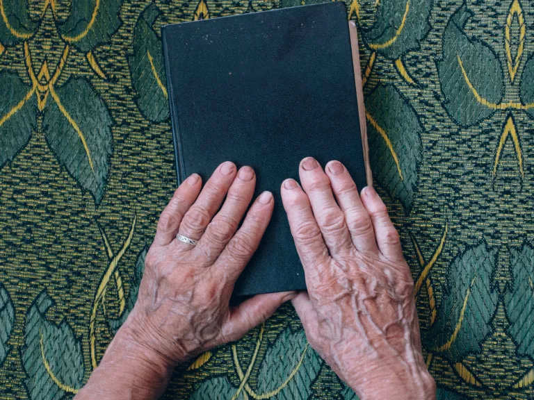 Aunt Dolores was constantly in her Bible studying, learning, and growing. She was also often in prayer, particularly for the trials that others were facing. Even in her deepest trials her heart and mind were on the needs of others. An older woman's hands resting on top of a Bible.