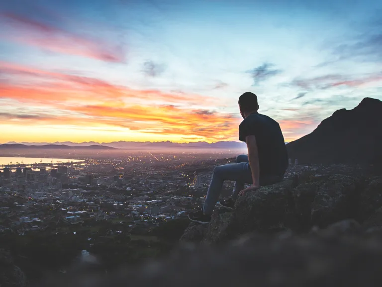 A young man sitting on a rock looking at the cityscape below.