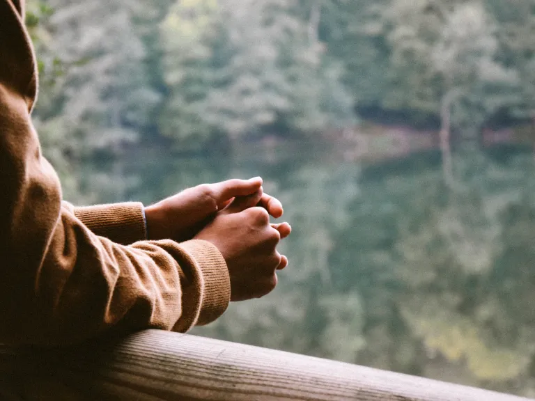 Our world is broken. There is so much pain and suffering. Our world is in need of intervention that only God can give. A person resting their arms on rail while looking out over a body of water.