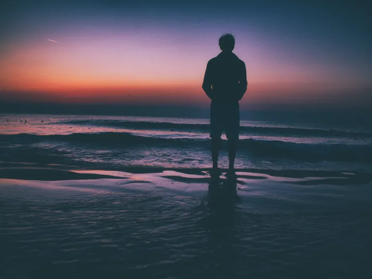 Dwelling on the past is of no help to anyone. We are to press forward toward the goal and not keep looking behind. A man standing by a lake at sunset.
