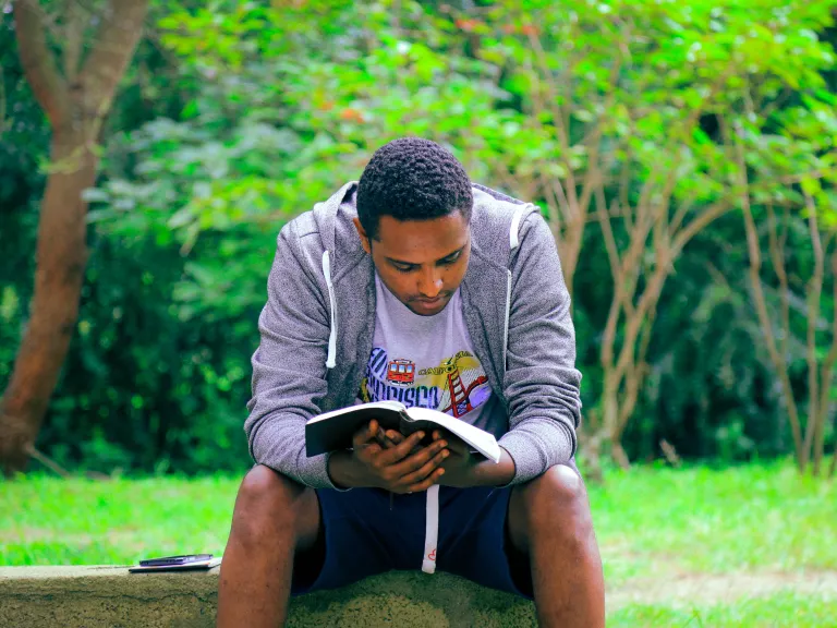 A man sitting on a bench reading a Bible.