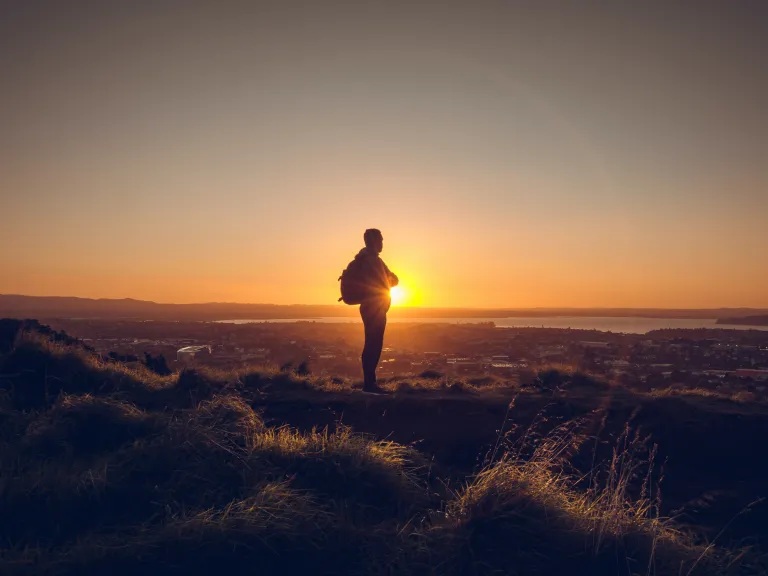 A man standing on a hill with the sun setting.