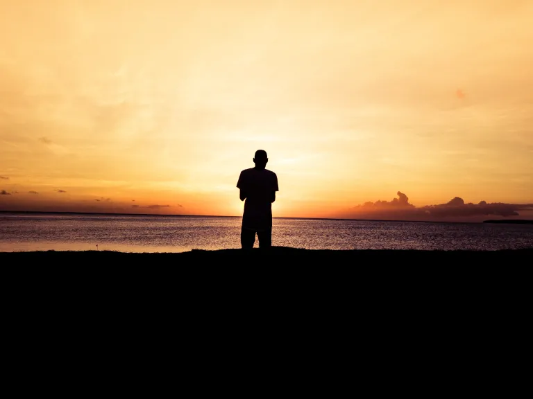 When God begins working with us, we start to see that our natural way of life—which appears well and good to us—leads spiritually nowhere. A person standing by a body of water at sunset.