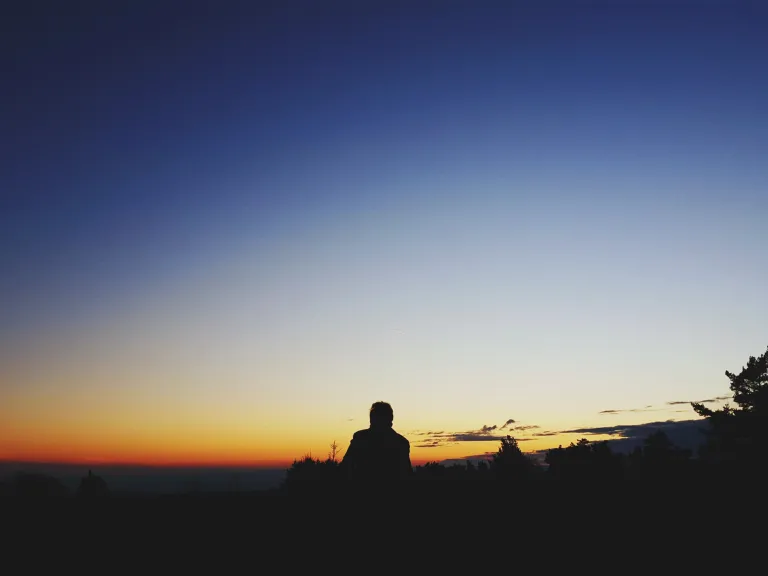 God has been working out a marvelous plan. A long, thoughtful and loving story has been unfolding right alongside the pain of human drama. A person sitting at the top of hill looking at the expanse of the night sky.