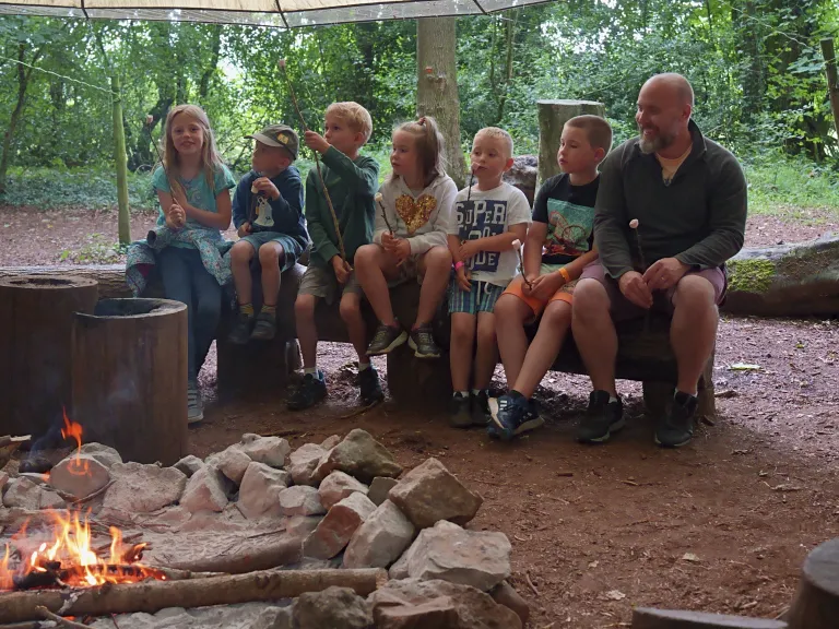 A group sitting by a campfire beneath a shelter