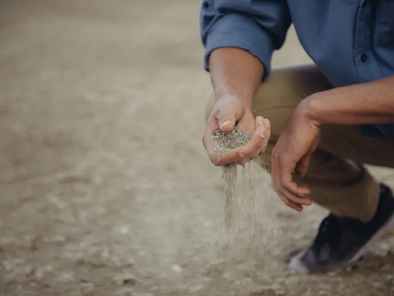a man crouching close to the ground and sifting grains through his hand.