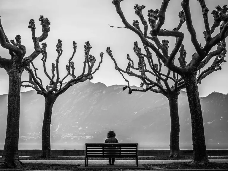 With God, we can be strong even though we may feel weak. When we are truly close to God, we will no longer feel as though we are facing life alone. A person sitting on a park bench in between two trees.
