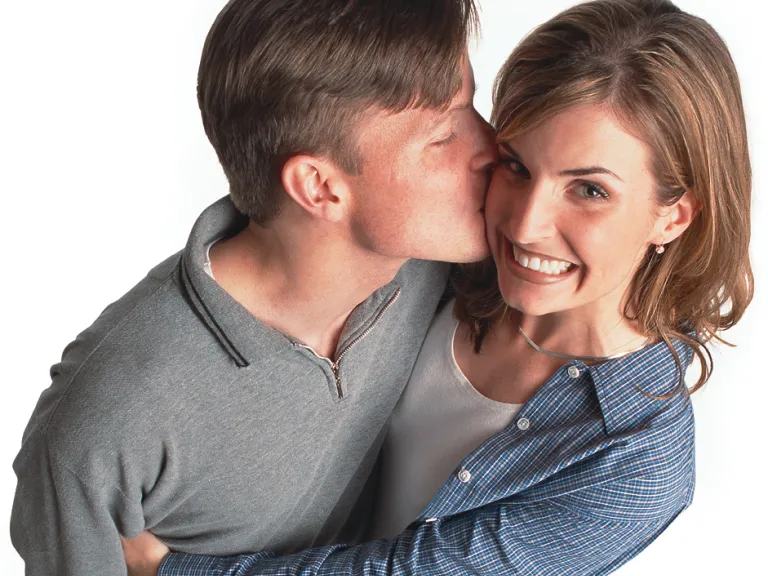 A young man kissing a young woman who is hugging him.