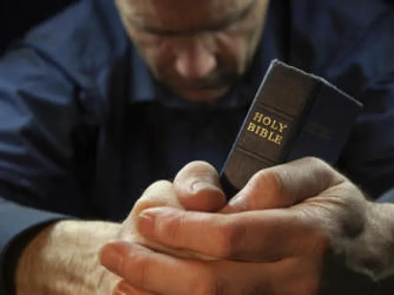 A man praying while holding a Bible.