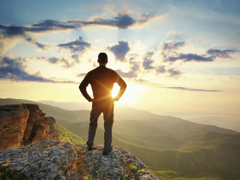 A young man on a cliff looking at the sunset.