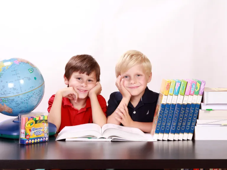 A homeschool co-op can be a much-needed resource for homeschooling parents who need subjects taught that are outside their comfort level or time available to teach. two boys with an open textbook on a desk alongside a globe and other school supplies