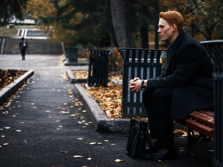 Though our flesh is weak and drawn to sin, true strength and deliverance come only through Jesus Christ. A man sitting on a park bench - thinking.