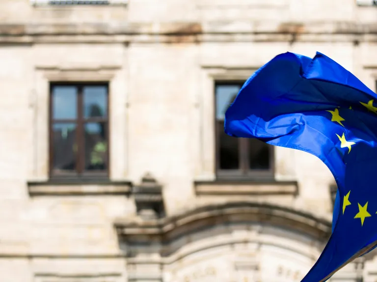 The European Union faces powerful winds of change—its future shaping rapidly as history, politics, and prophecy converge. A European Flag blowing in the wind outside of an old building.