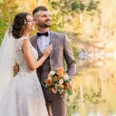 a man and a woman in wedding attire outdoors with a lake in the background