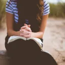 a woman sitting with folded hands on an open Bible