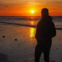 A young man walking on the beach while the sun is setting.