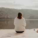 A woman sitting on a dock looking out over a lake.