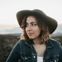 a woman wearing a hat and denim jacket standing outside and looking to her side
