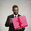 A man holding a wrapped gift looking at it.