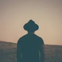 A man wearing a hat looking out over a grassy field.