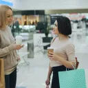 two women in a mall holding shopping bags and talking with one another
