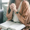 A woman with a Bible in her lap with clasped hands praying.