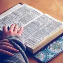 A woman with an open Bible laying on a table.