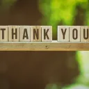 blocks spelling "thank you" balanced on a ledge against a backdrop of trees