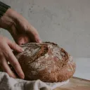 a pair of hands placing a loaf of bread onto a wooden cutting board
