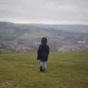 Child in black jacket walking on grass field during daytime.